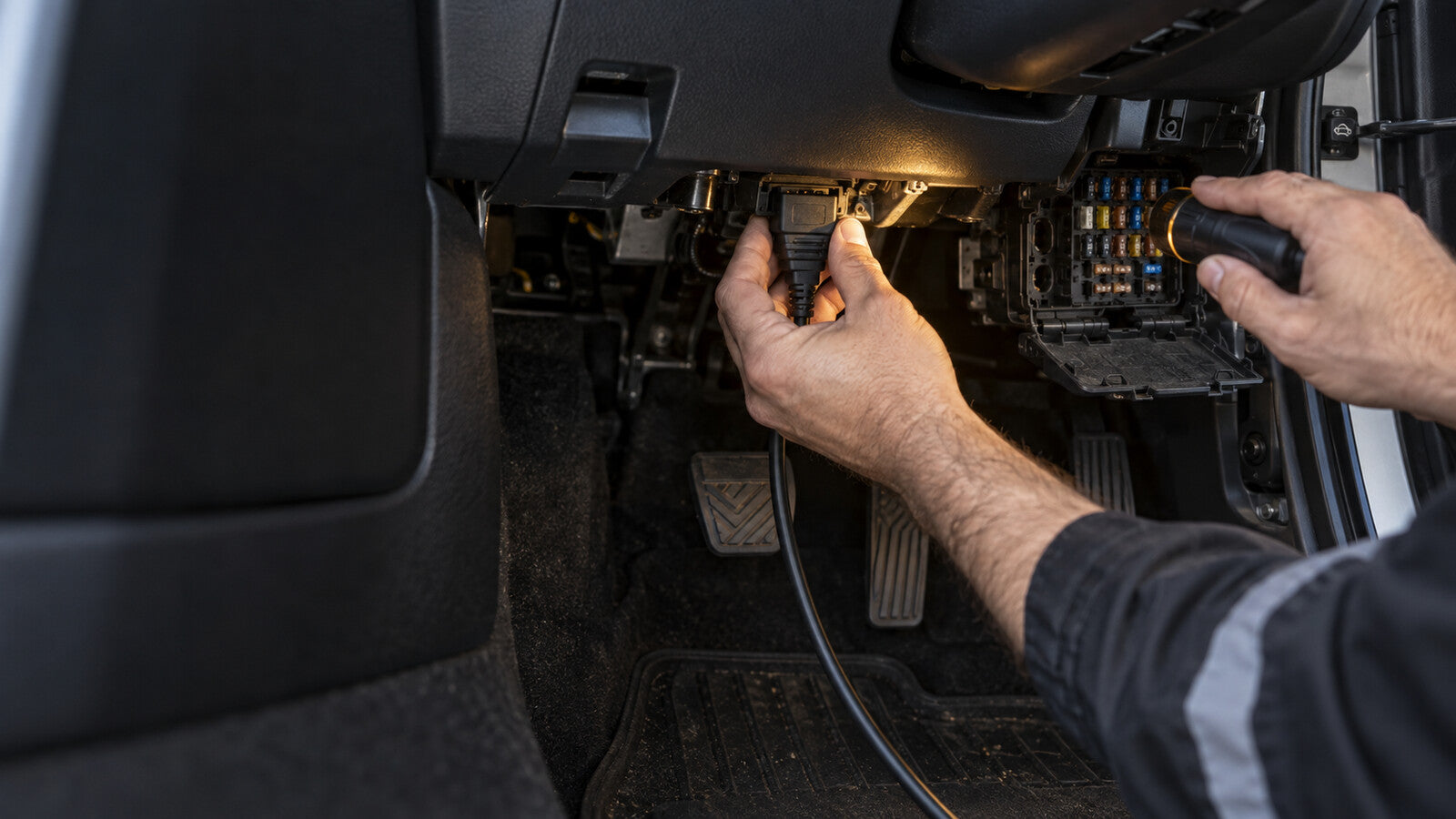Technician checking an OBD diagnostic connector and fuse area in a vehicle footwell