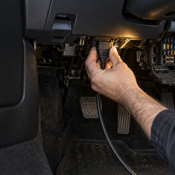 Technician checking an OBD diagnostic connector and fuse area in a vehicle footwell